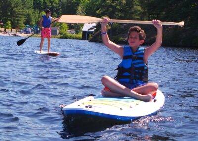 A boy is riding a paddle board in the water.