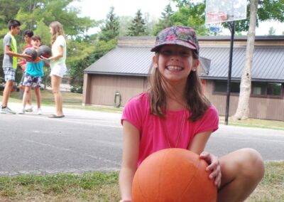 A young girl sitting on the ground holding a basketball.