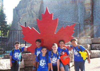A group of kids posing in front of a canadian flag.