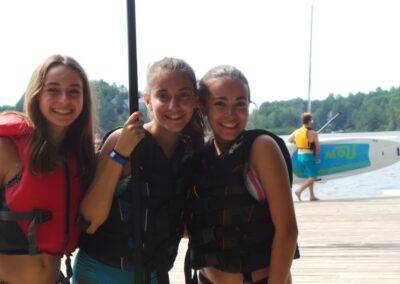 Three girls in life jackets posing for a photo on a dock.