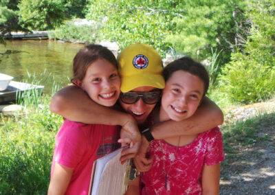 Three girls hugging each other near a lake.