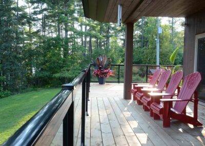 A deck with red adirondack chairs on it.