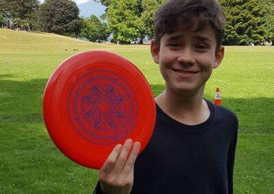 A boy holding a red frisbee in a park.