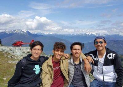 Four young men posing in front of a mountain with a helicopter in the background.