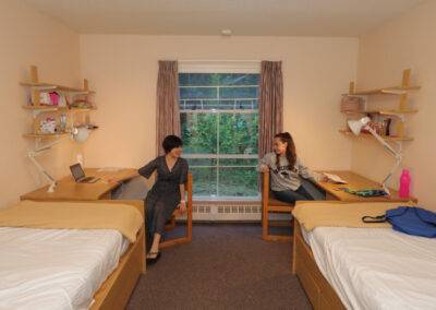 A dorm room with two beds and a desk.