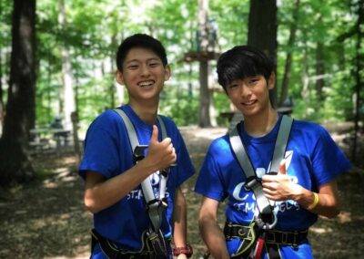 Two boys in blue shirts standing next to each other in the woods.