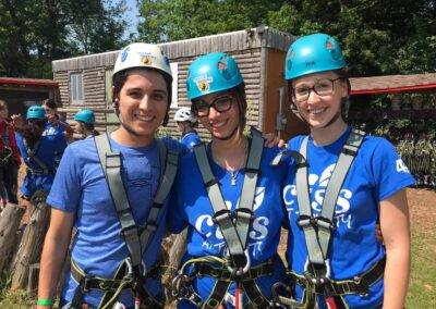 Three people in blue shirts standing next to each other on a ropes course.