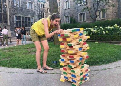 A girl playing with a stack of wooden blocks in front of a building.
