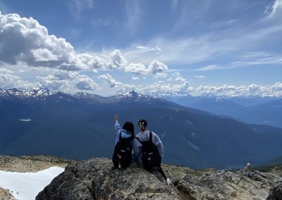 Two people sitting on top of a mountain overlooking the mountains.