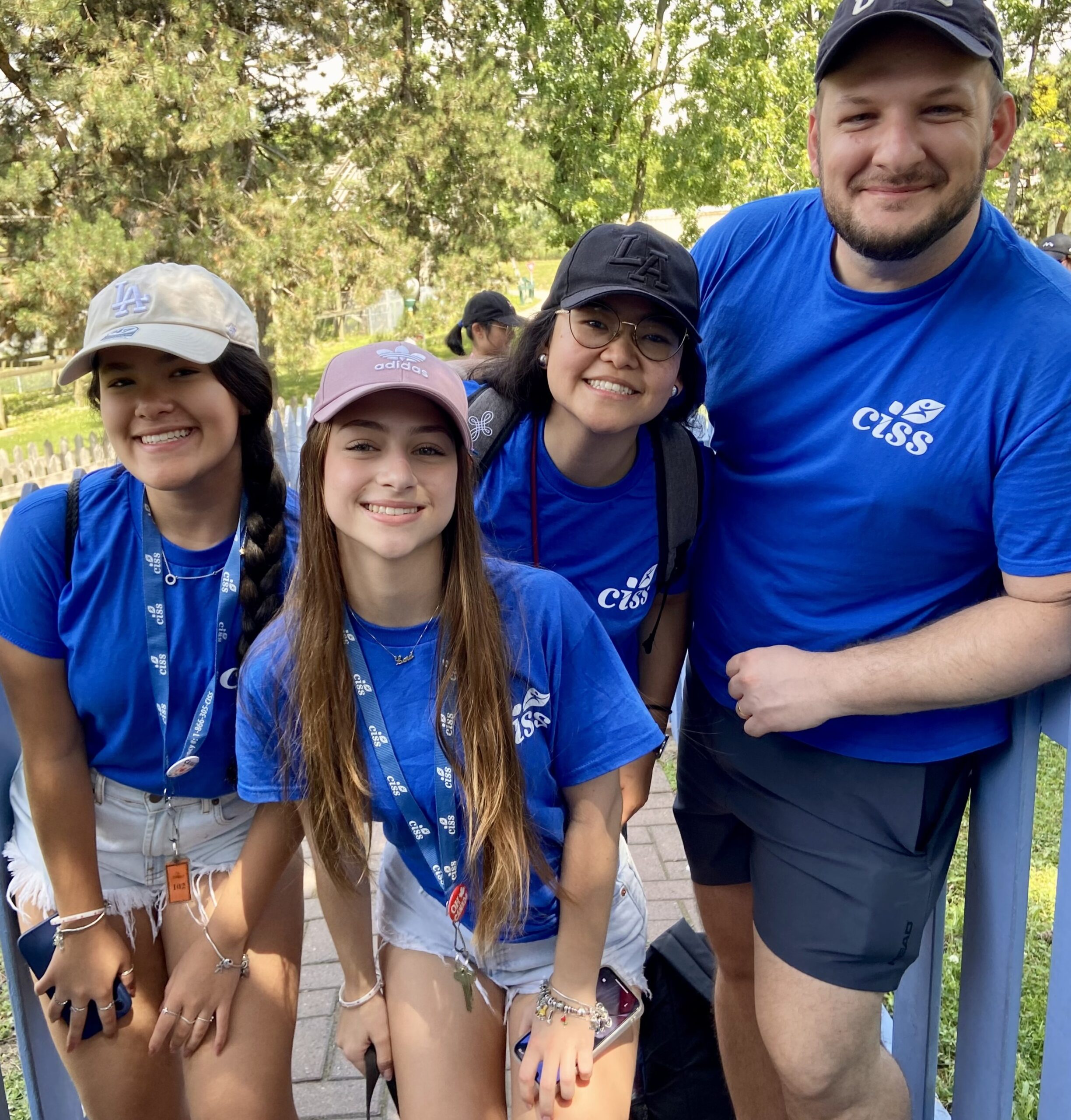Four people in matching blue CISS t-shirts and baseball caps posing outdoors.